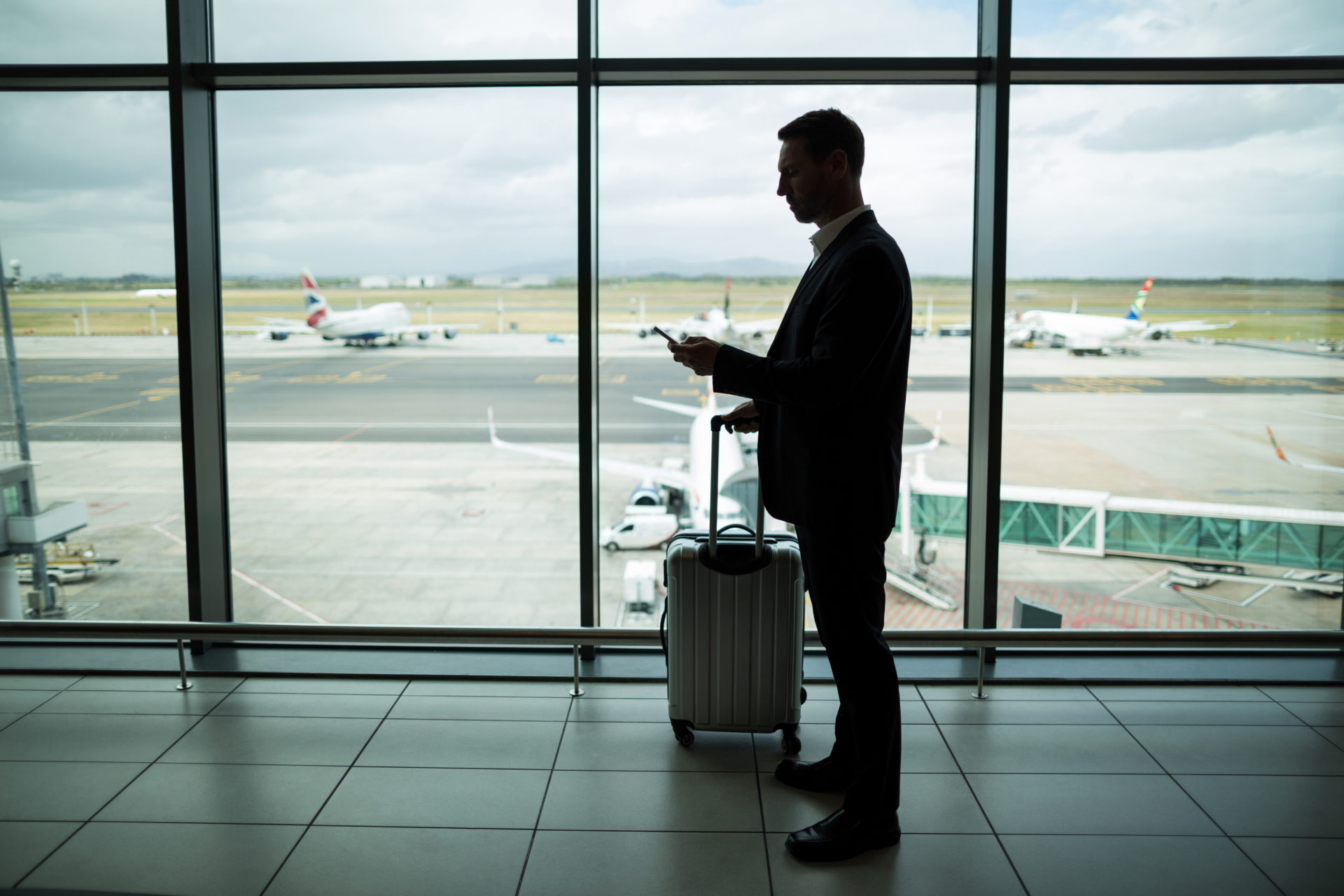 Businessman With Luggage Using Mobile Phone At Airport